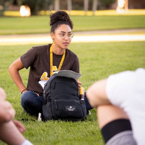 A woman sitting on grass with a backpack.