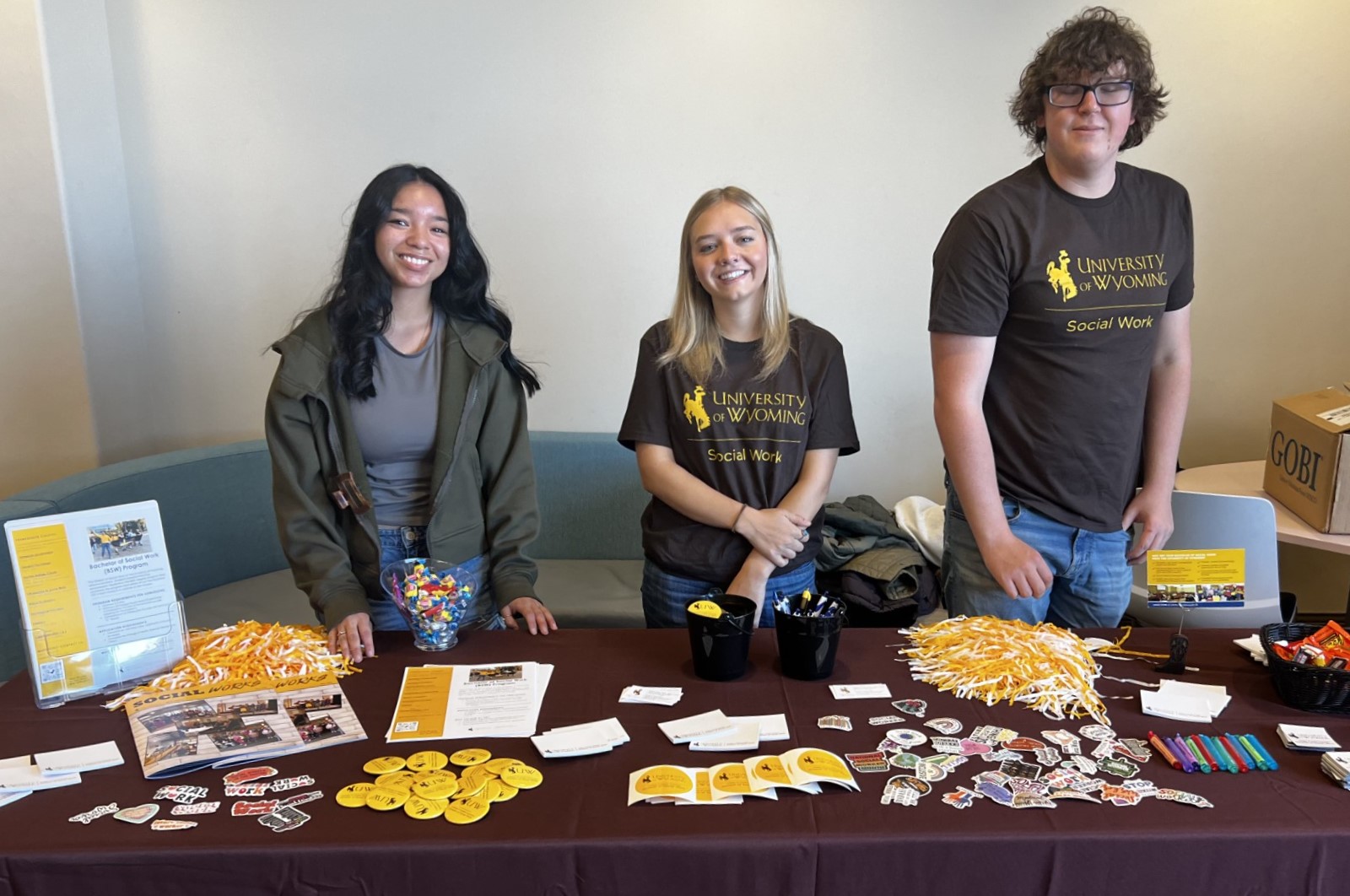 Three people stand behide a table with promotional materials.