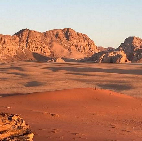A red sand desert with a rock formation in the far background 