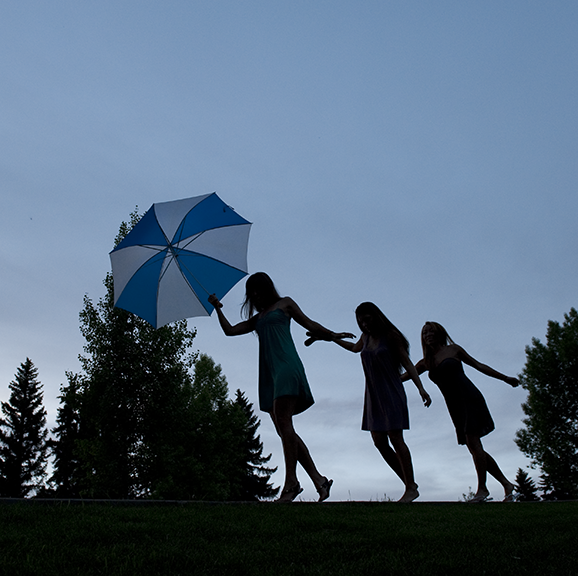 Backlit group of 3 women walking with an umbrella at sunset