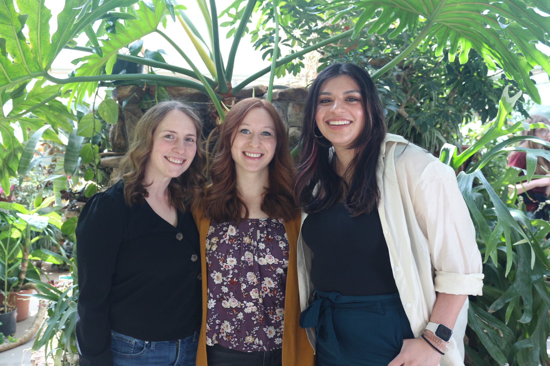 Three students smiling under a tree.