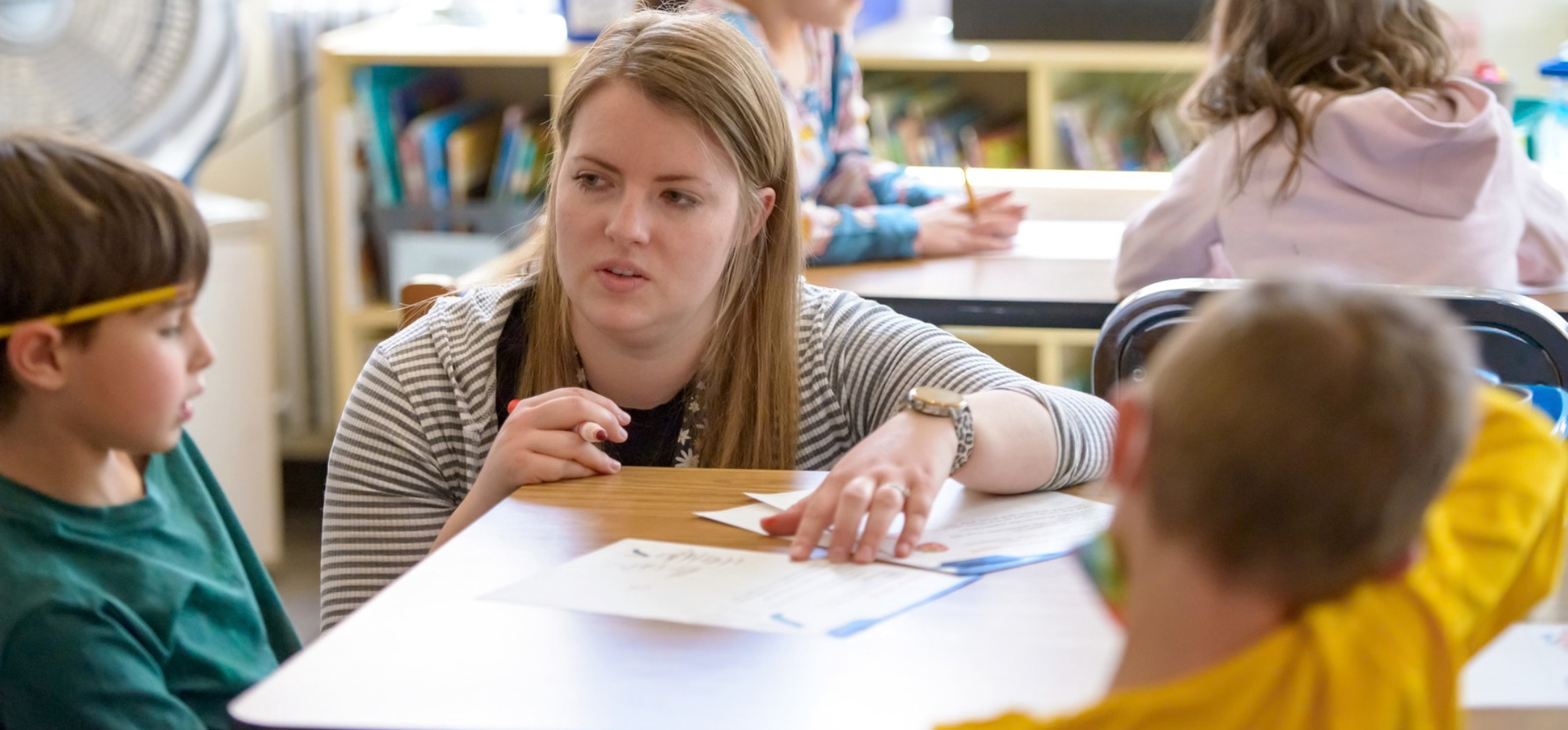 A woman working with students in her elementary classroom
