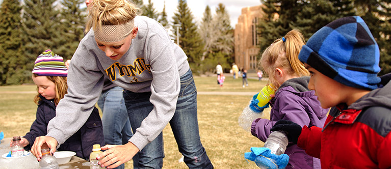 A pre-service teacher plays with young children on Prexy's pasture