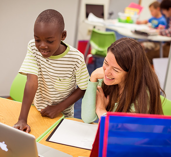 Student showing teacher something on laptop