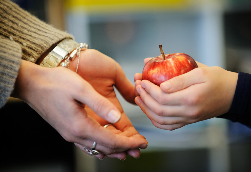 A child hands an apple to their teacher