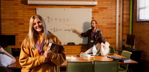 A UW student holds a book and smiles for the camera while students work on coursework in the background at the STEP Tutoring Center.