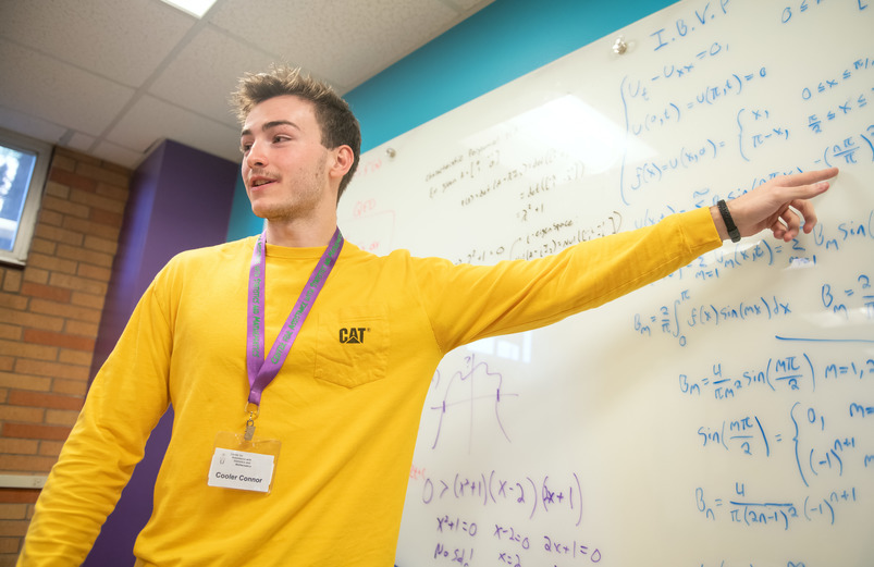 A UW student works as a STEP tutor, explaining a math problem on the whiteboard.