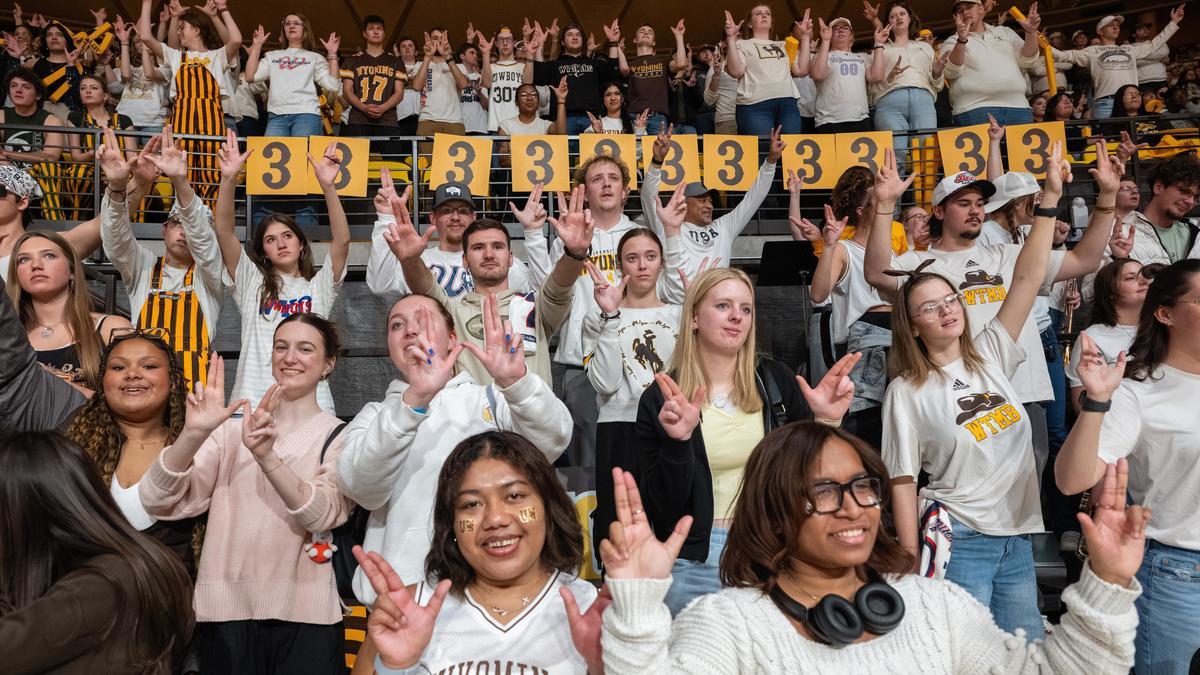 Several students hold up the "W" sign with their hands at a UW basketball game