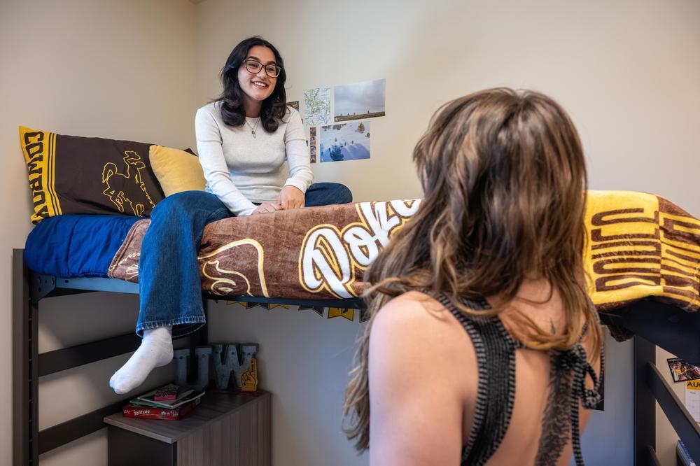 Two students sit, smiling, on the top bunk of a UW residence hall