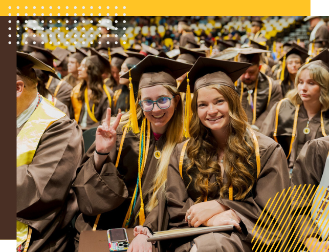 Two graduates smile for a photo at Commencement