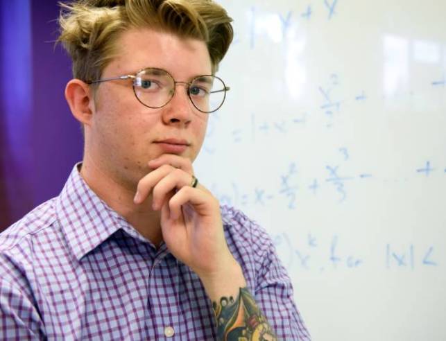 Student standing in front of whiteboard with math equations on it.