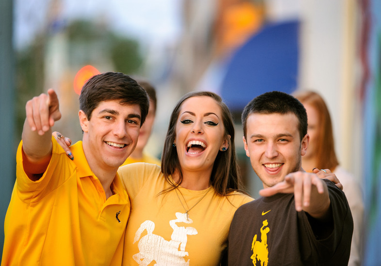Three students smiling and pointing at the camera