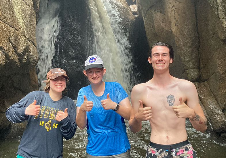 Three students pose in front of a waterfall