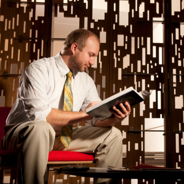man in shirt and tie sitting in ed annex looking at a book