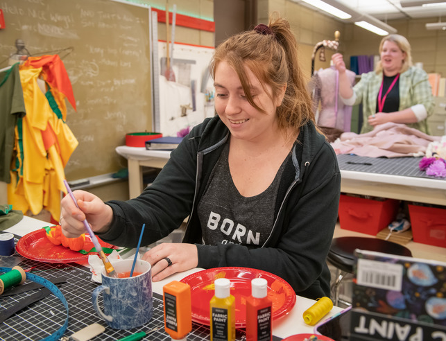 A student paints a display for the theatre & dance department.