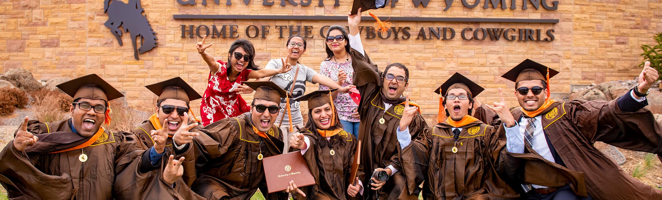 Several students pose in front of the main sign for the University of Wyoming, "Home of the Cowboys and Cowgirls."