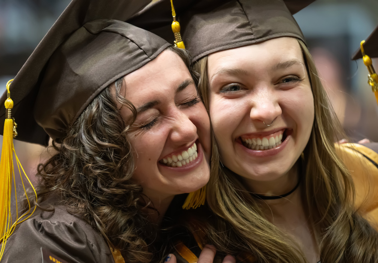 Two UW students smile at a University of Wyoming graduation ceremony.