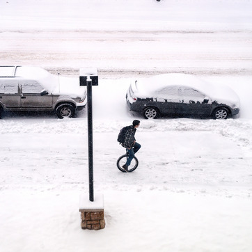 Student Unicycling next to Parked Vehicles