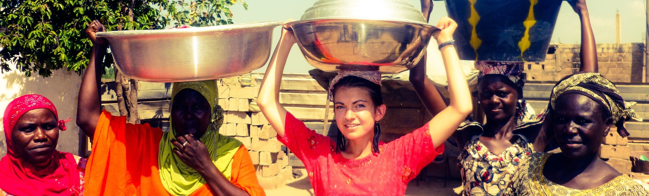 A female UW student in the middle of other African females carrying a heavy load of something in jars on their heads.