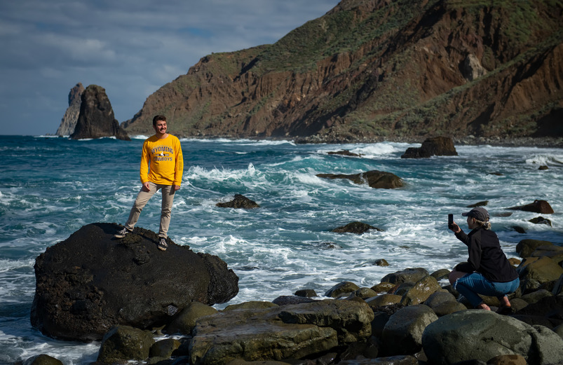 A UW study abroad student stands on rocks next to the ocean.