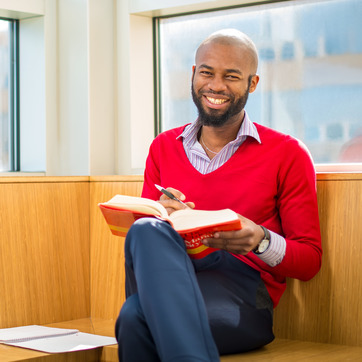 Student reading and smiling by a window