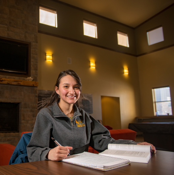 a student taking notes and smiling at the camera