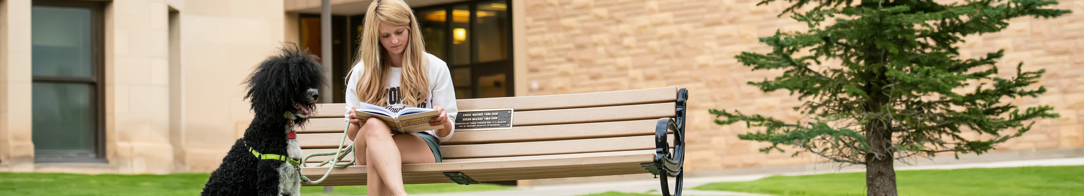 Student and her dog reading on a bench on campus