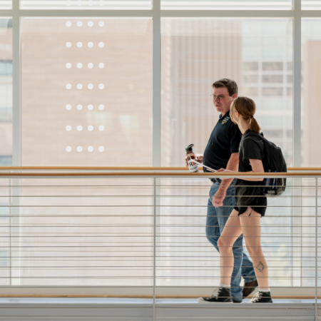 two people walk in front of large windows