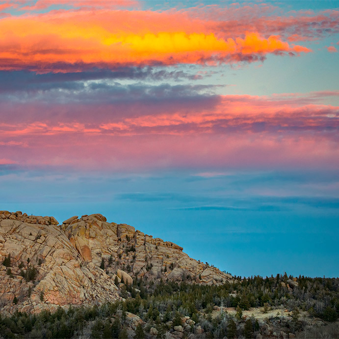 a landscape at dusk with a blue and orange sky, rock formations, and trees