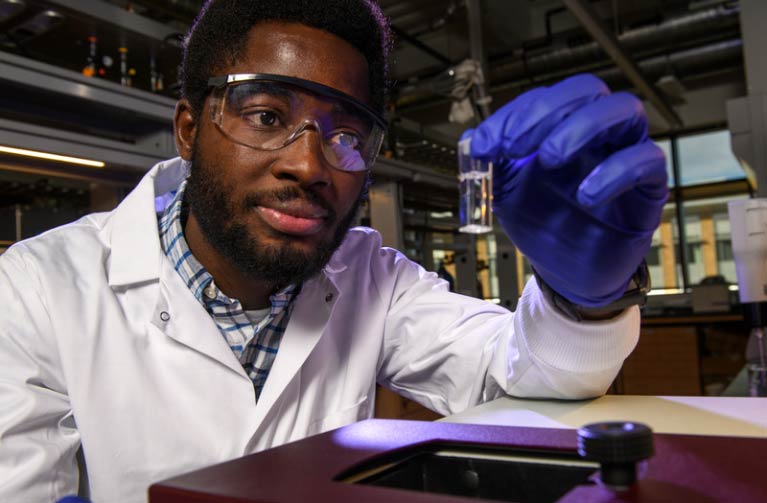 student in lab equipment looking at a test tube