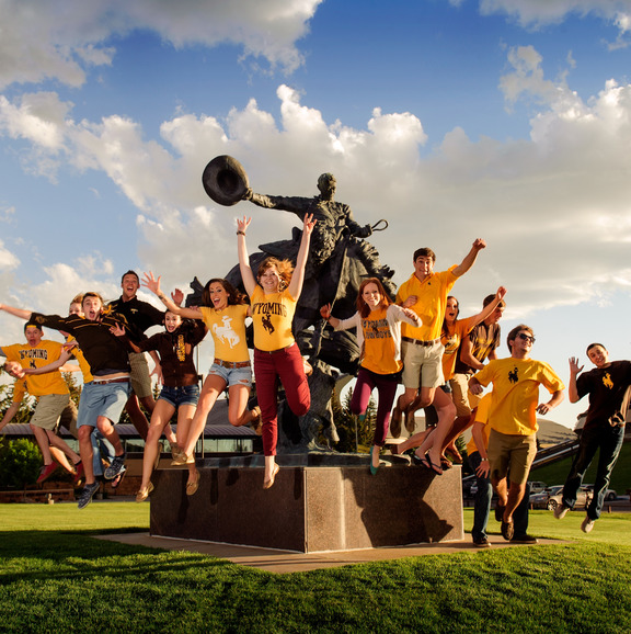 students jumping in front of a steamboat statue 