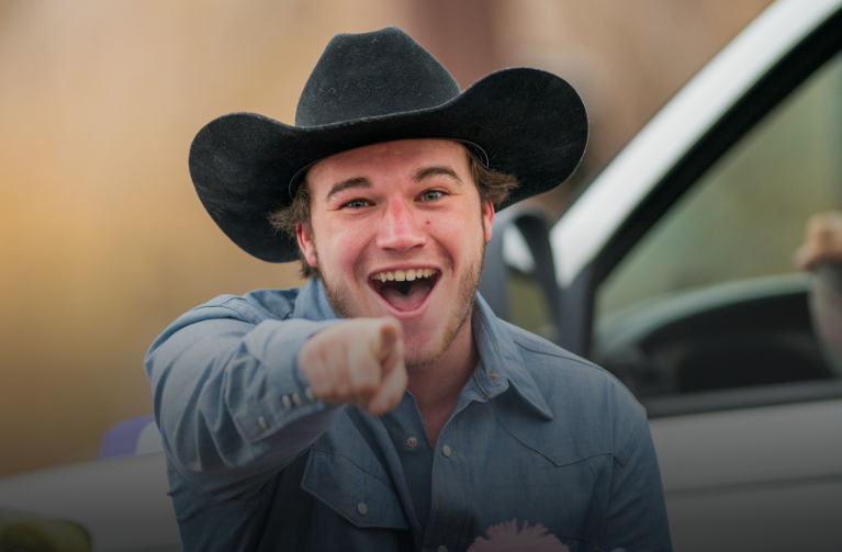 Student in a cowboy hat pointing at camera and smiling during parade
