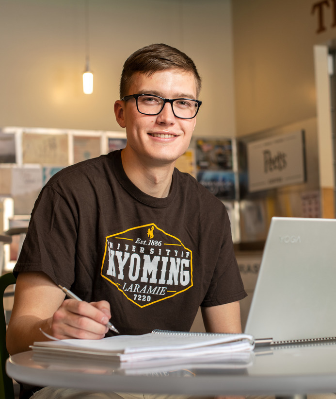 A student in a coffee shop doing work on their computer and notebook