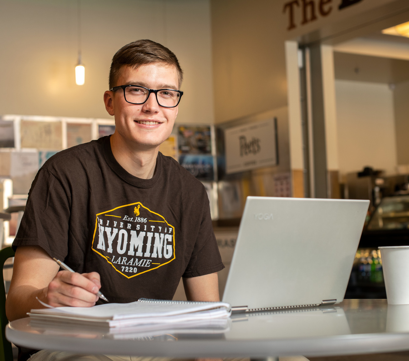 Student in coffee shop doing work on their computer and notebook