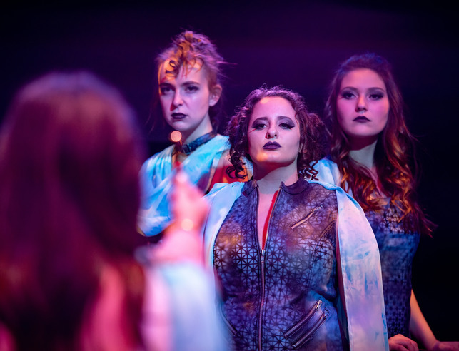 Three students stand together during a theatre performance in a scene