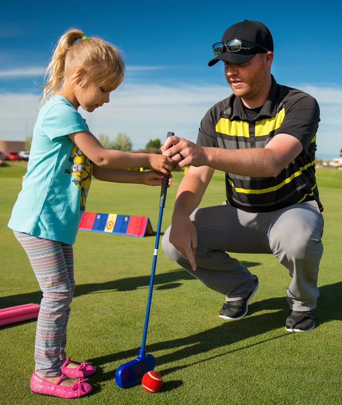 Teacher helping young student golf.
