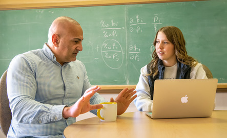 A professor talks to a student working on their laptop