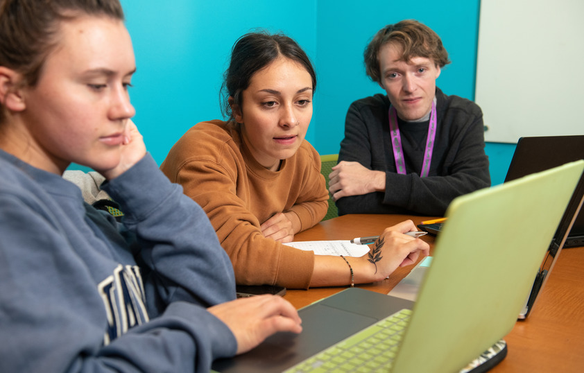 Three students look at a computer together.