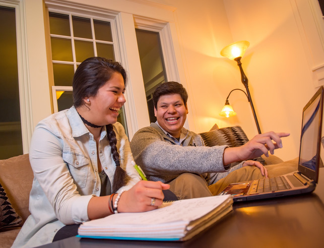 Two students laugh while studying together on a couch