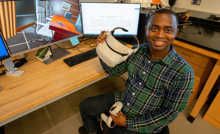 A student smiles for a photo while holding a V.R. headset