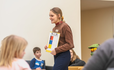 An art teacher is smiling as a group of children listen