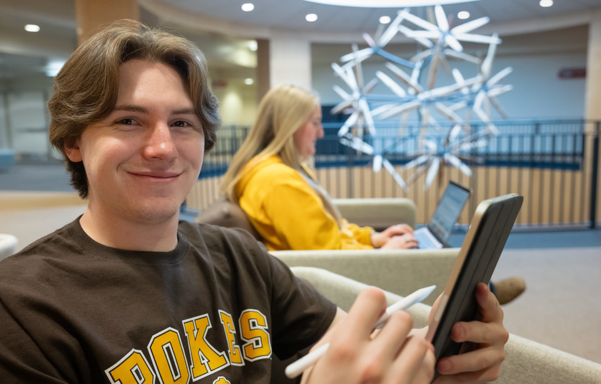 Student with a tablet in hand smiles at camera