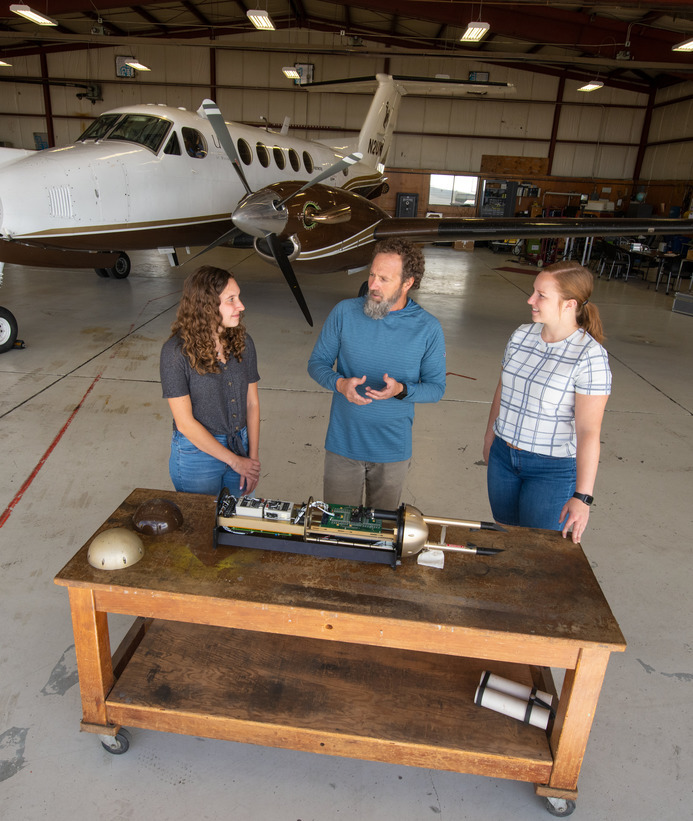 Professor teaching two students about an airplane part