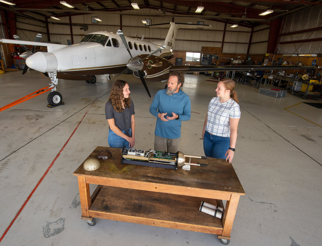 Professor teaching two students about an airplane part