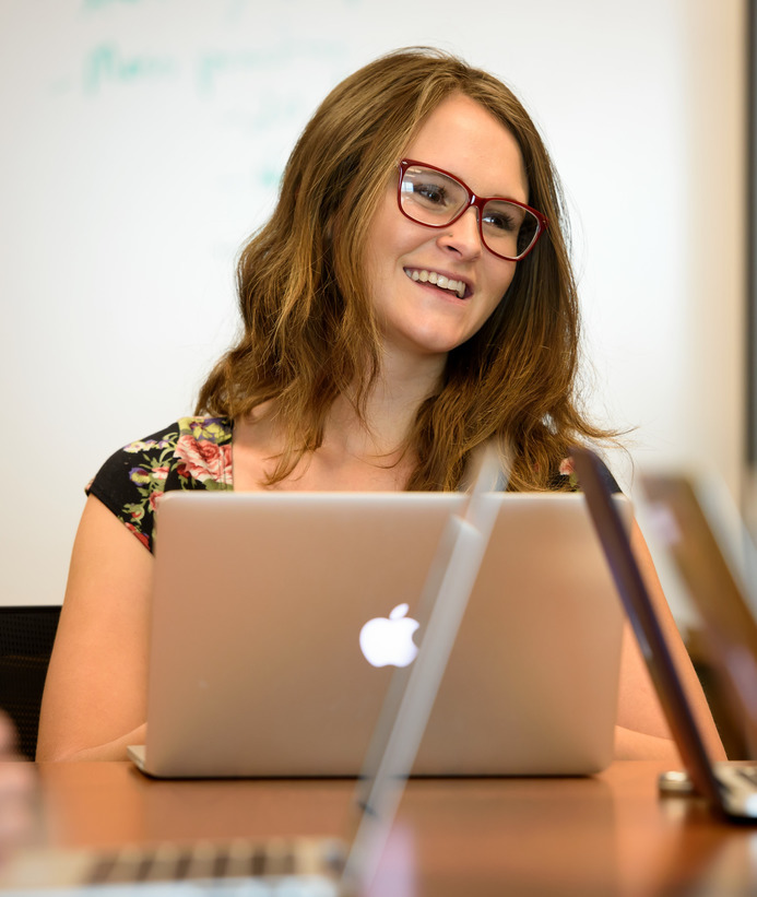 A student smiles while sitting at a table with her laptop open