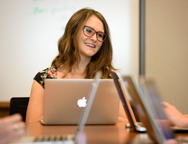 A student smiles while sitting at a table with her laptop open