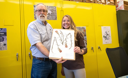 A student and a professor hold up a botany project