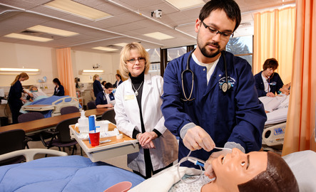 A student works on a fake body in front of a professor