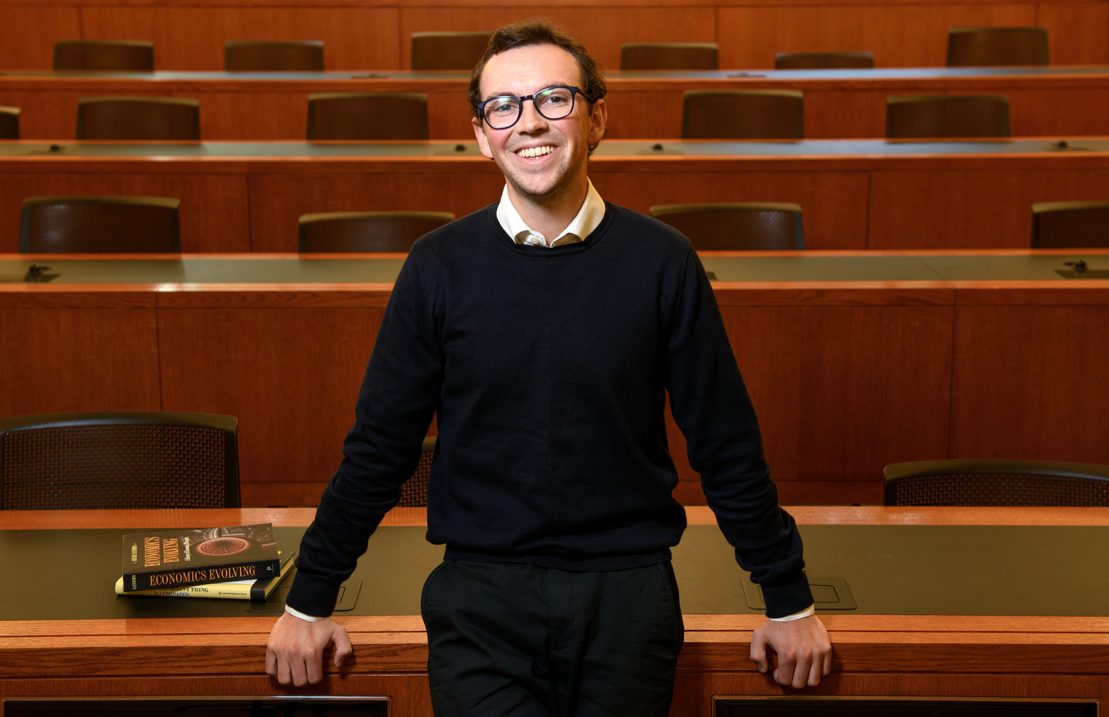 A student stands in front of wood paneling.