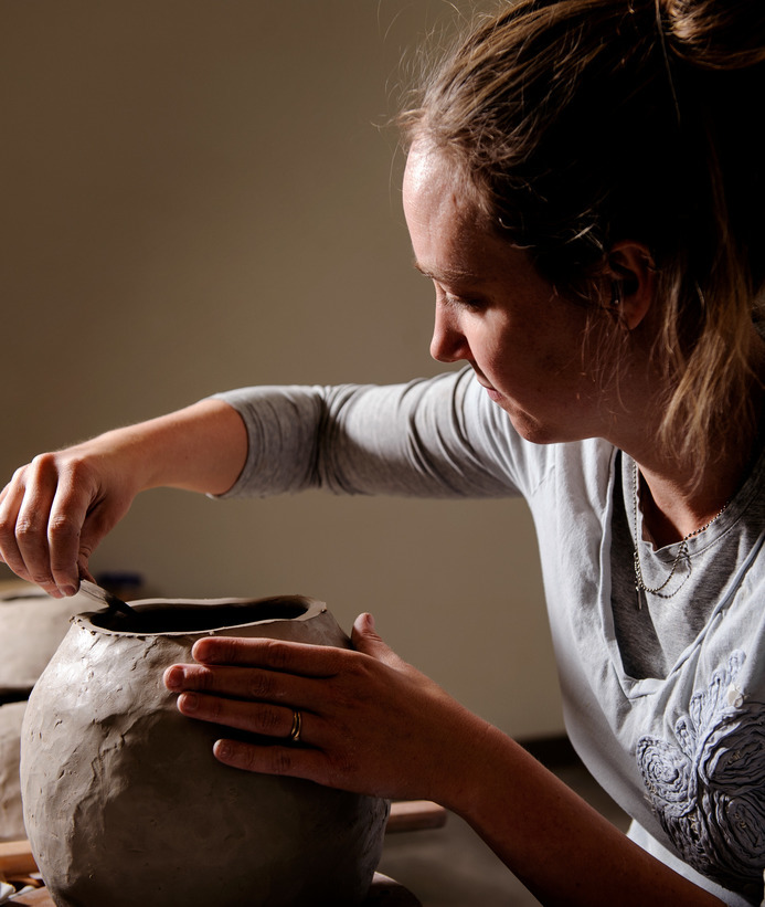 Ceramics student sculpting the top of a clay vase